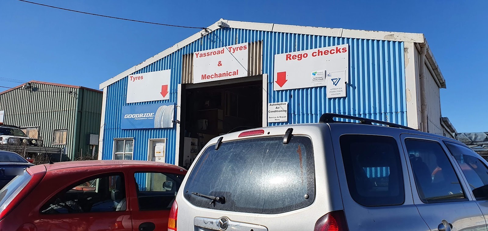 Cars parked outside the shed under the Yassroad Tyres sign
