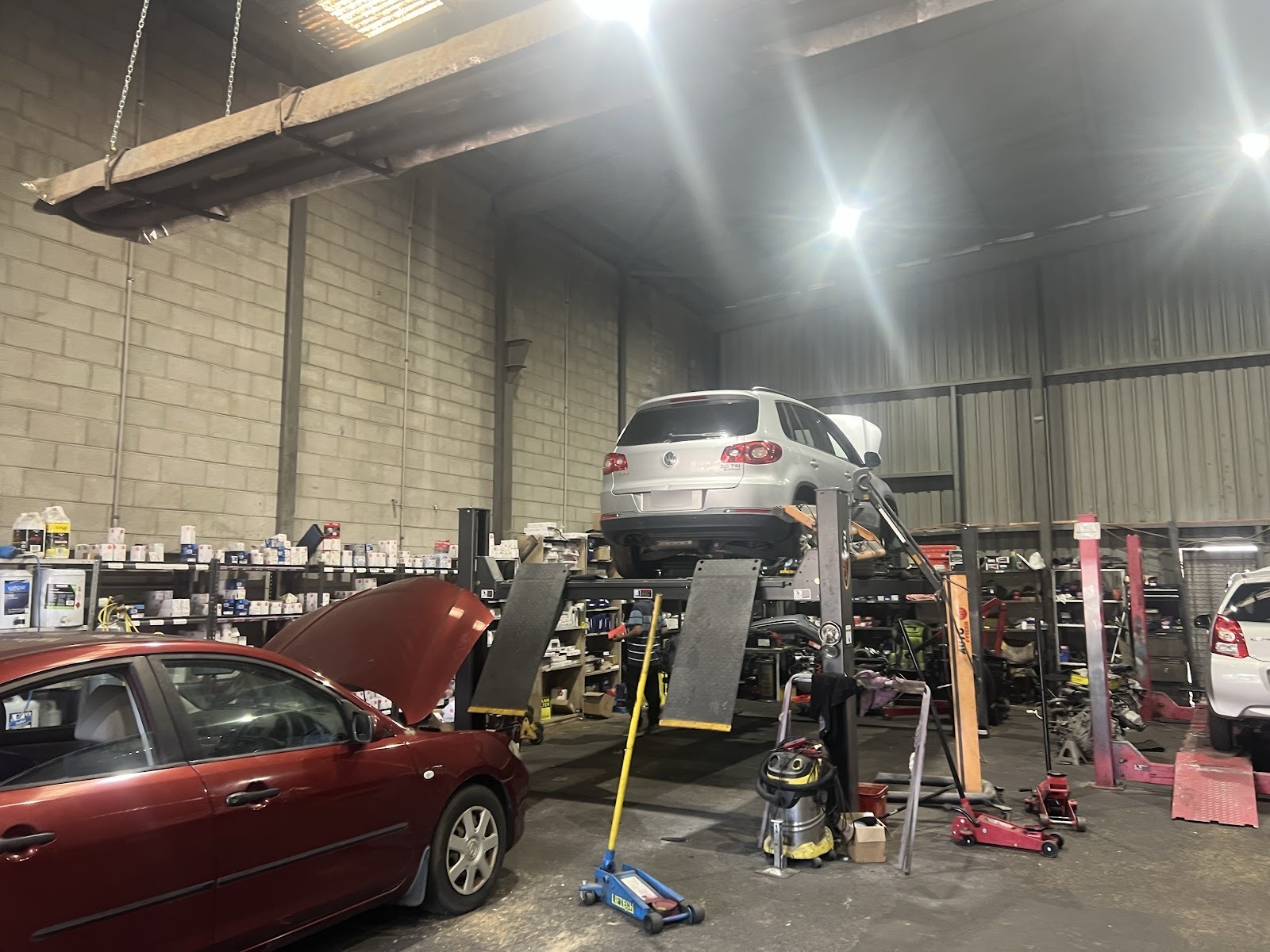 An SUV up on the four-post hoist with a car in for repairs beside it